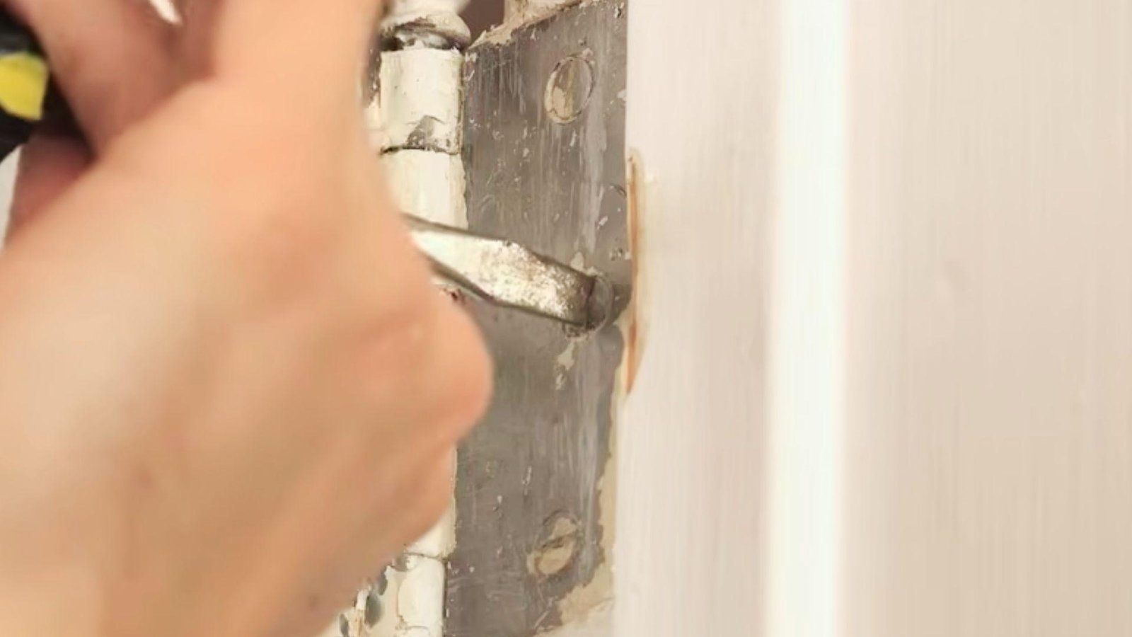 Using a screwdriver to tighten loose hinge screws on a white interior door.