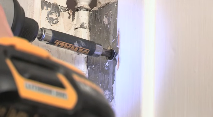 Driving a longer screw into a door hinge with a power drill to improve door alignment.