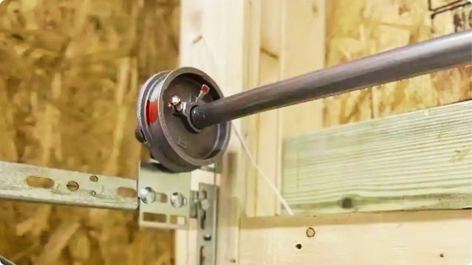 Close-up of a garage door cable drum and torsion spring assembly mounted above the door.