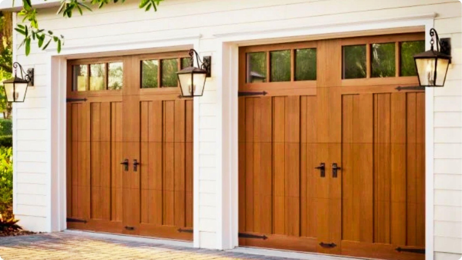 Carriage-style wood garage doors with glass window panels and black hardware on a white exterior.
