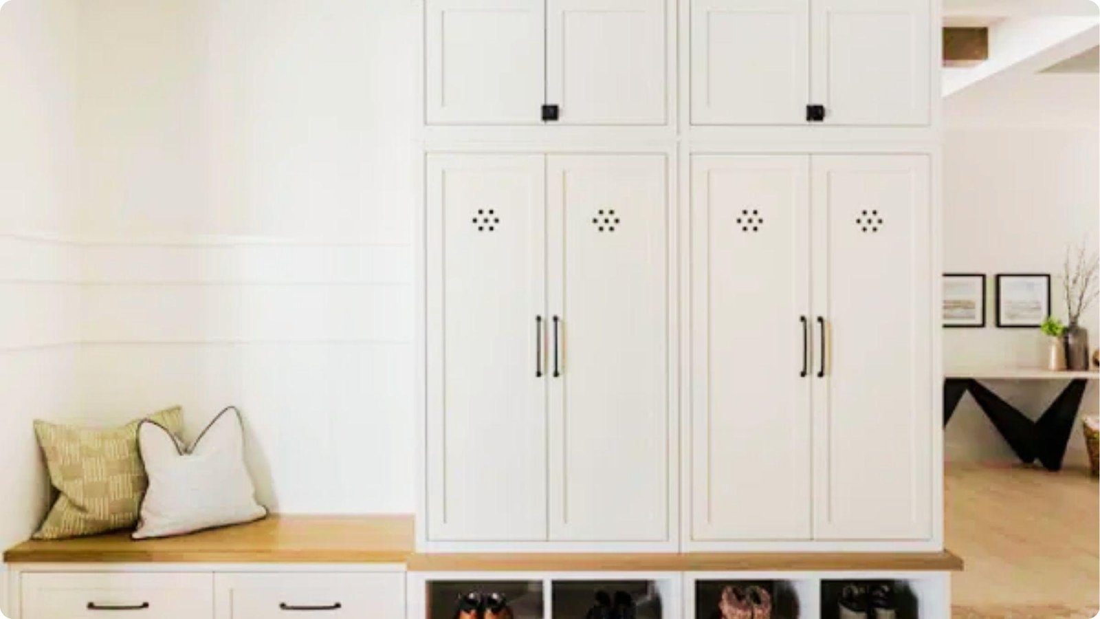 All-white mudroom featuring tall lockers, cushioned bench, and open shoe cubbies below.