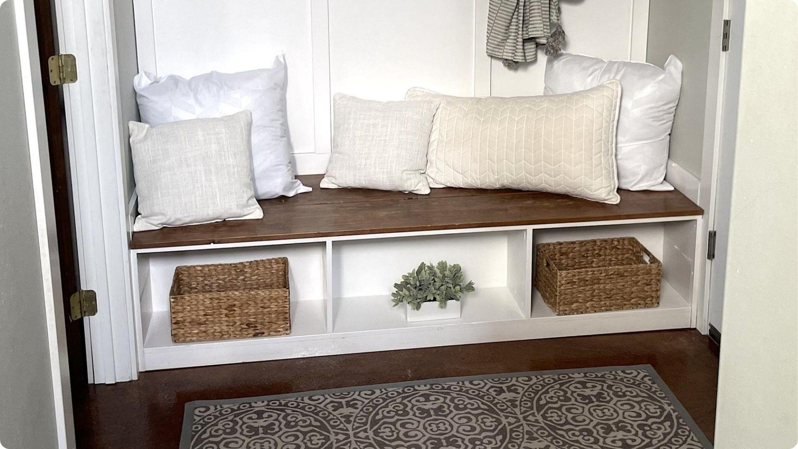 Built-in garage mudroom bench with wood seat, white cubbies, and woven baskets underneath for hidden storage.