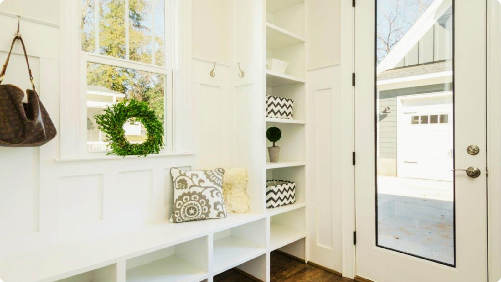 Sunny white mudroom with built-in bench, open shelving, and glass-paneled doors to the outside.