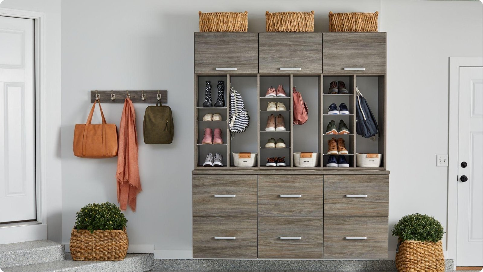 Organized garage mudroom with wood-tone storage unit featuring shoe cubbies, backpack hooks, and overhead cabinets.
