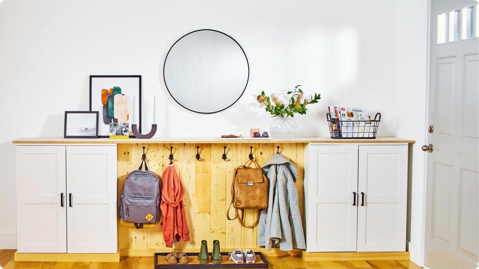 A built-in entryway solution with white storage cabinets flanking a wood slat panel with black hooks for bags and coats.