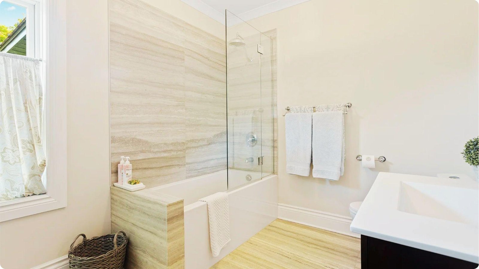 Bright bathroom with a frameless half glass shower screen on a bathtub and wood-look tile flooring.