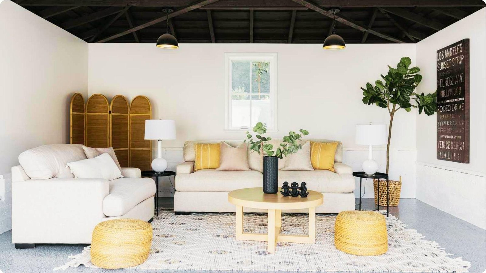 Converted garage lounge with white sofas, yellow accent pillows, and rattan stools on a patterned rug.