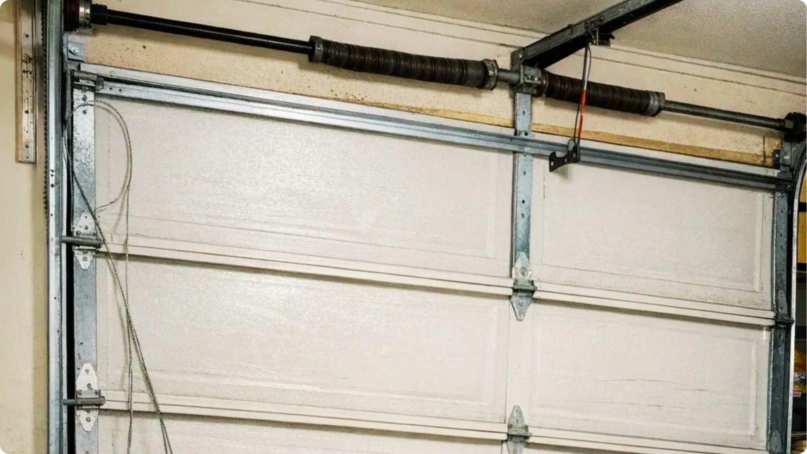 Interior view of a white garage door with a broken lift cable hanging loose on the left side.