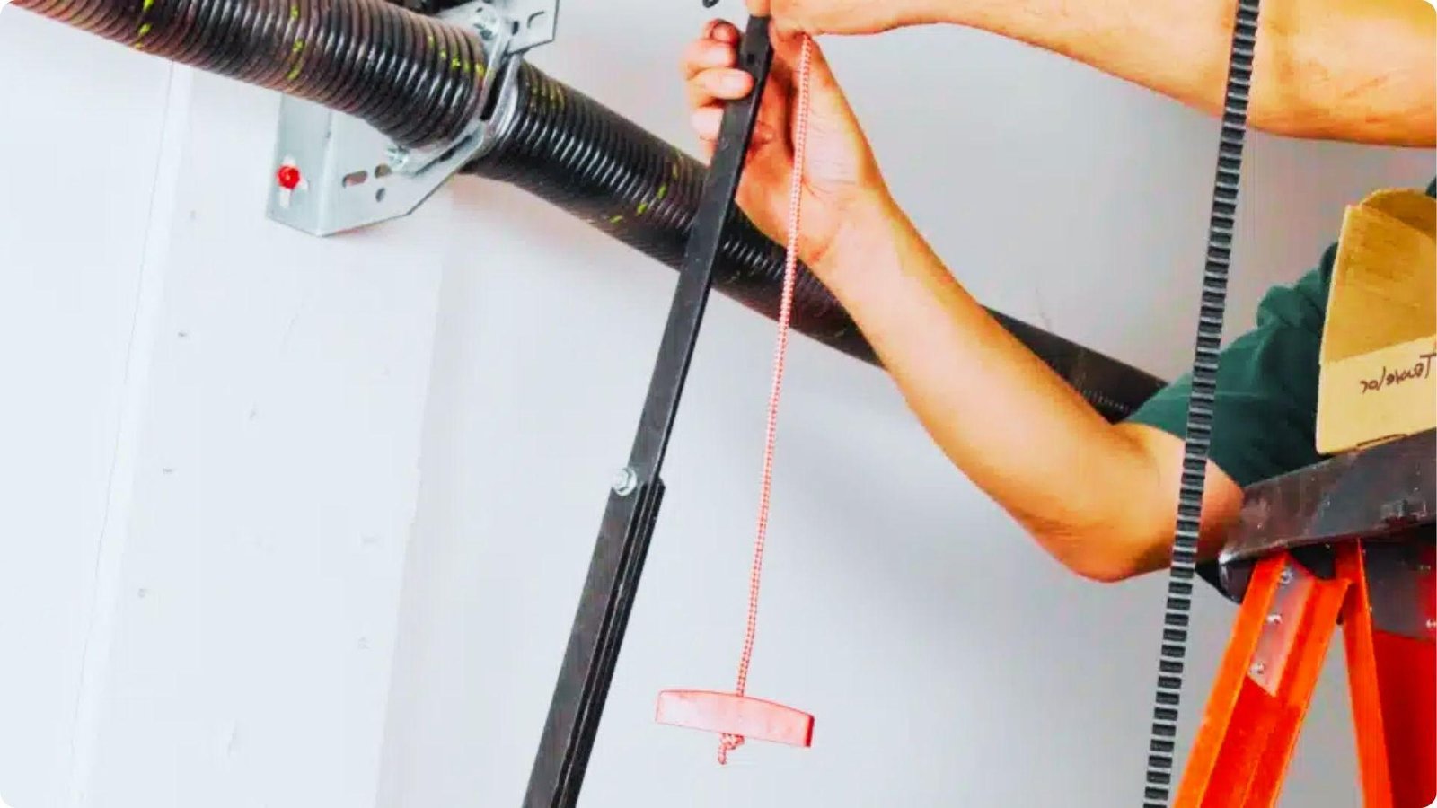 A person on a ladder releases the garage door opener’s emergency cord near the torsion spring.