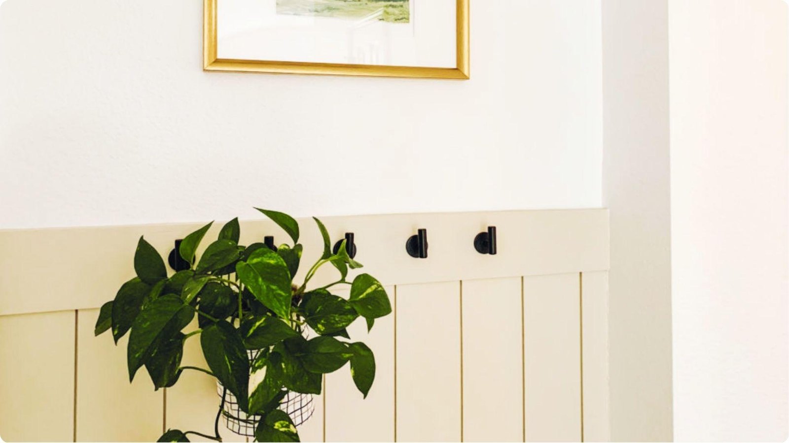 Minimalist garage entry wall with white paneling and black metal hooks for hanging items.