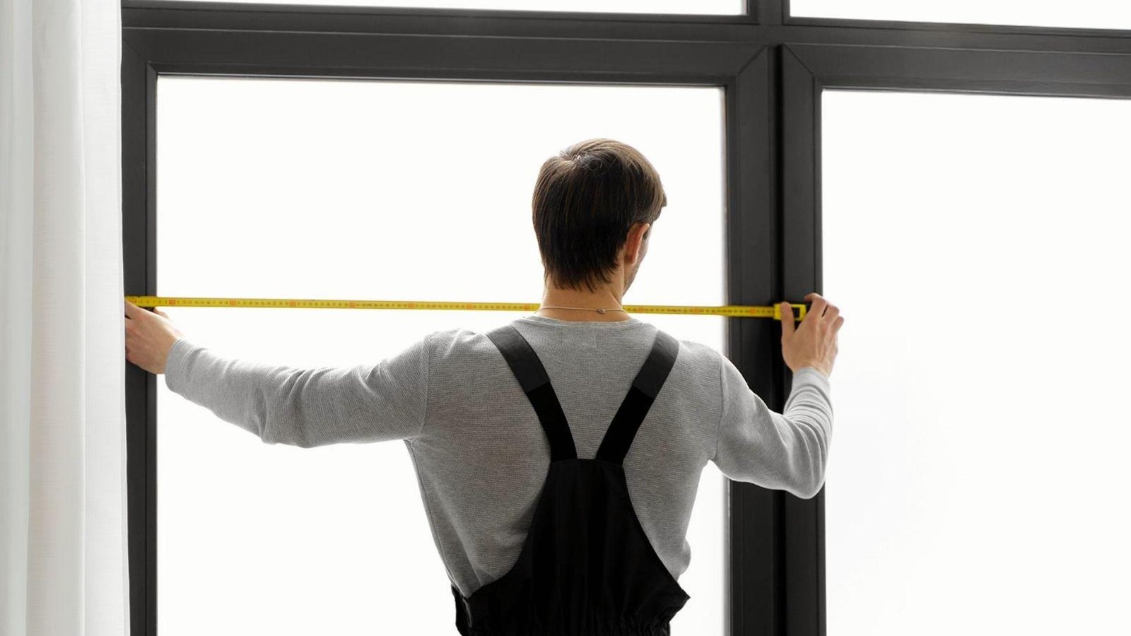 Contractor measuring width of black door frame with tape measure to determine correct bifold door rough opening