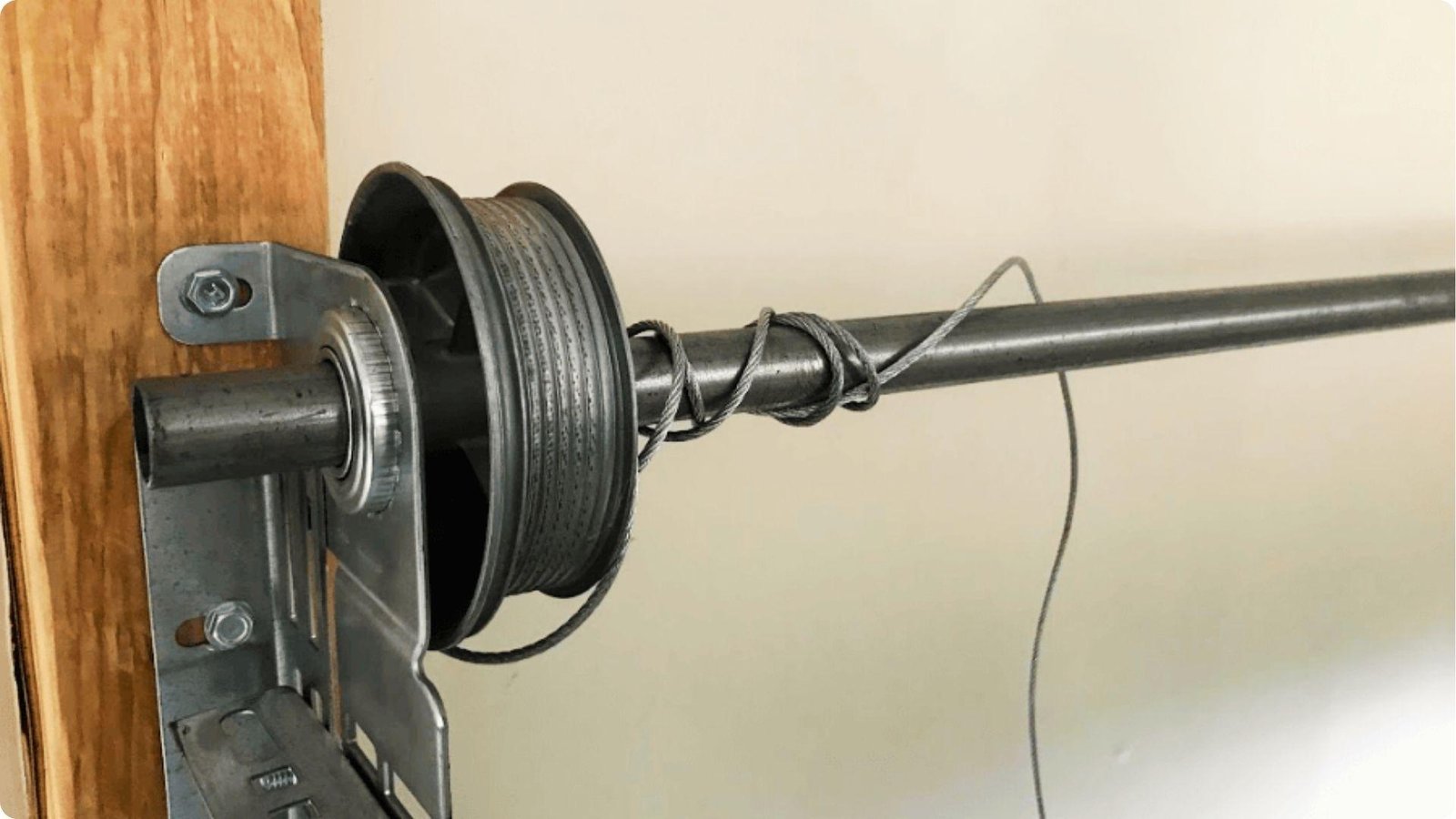 A broken garage door cable is tangled around the torsion bar and slipping off the cable drum.