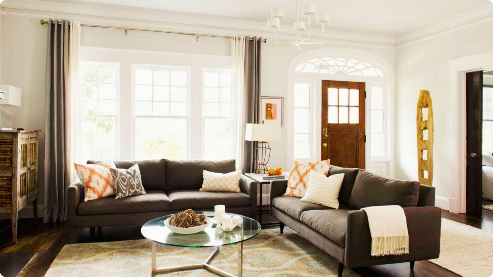 A living room with gray sofas is separated from the front door using furniture placement and a sculptural decor piece.