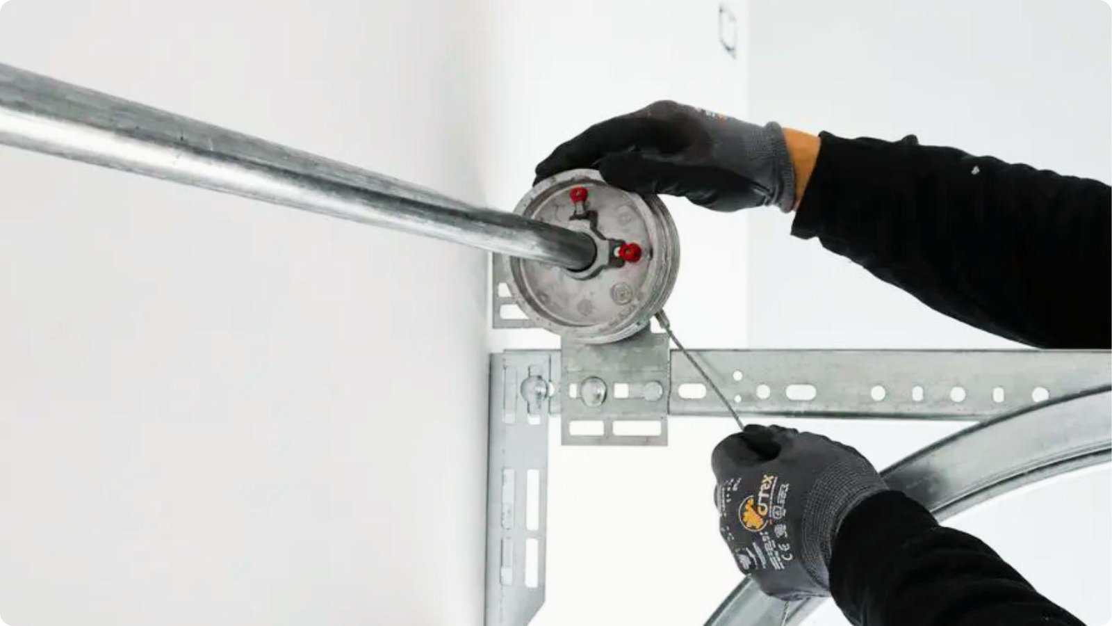 Gloved hands feed a new garage door lift cable through the cable drum on the torsion bar.